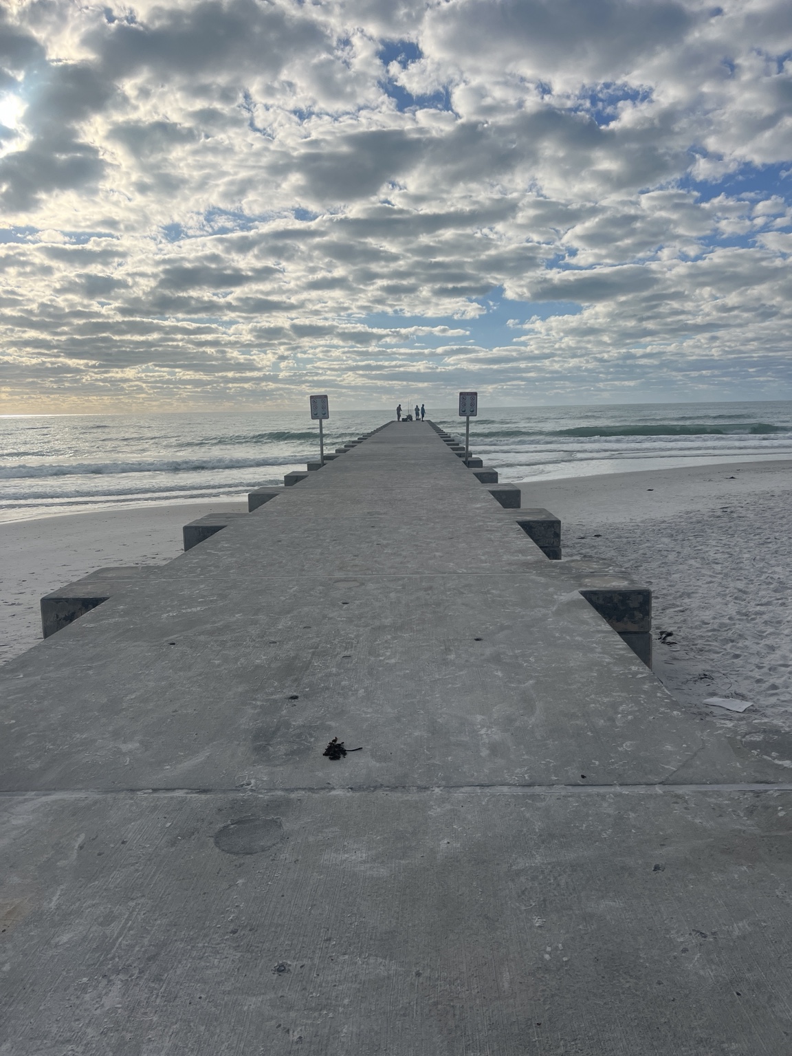 A concrete pier stretching toward the Gulf beneath dramatic clouds on Anna Maria Island