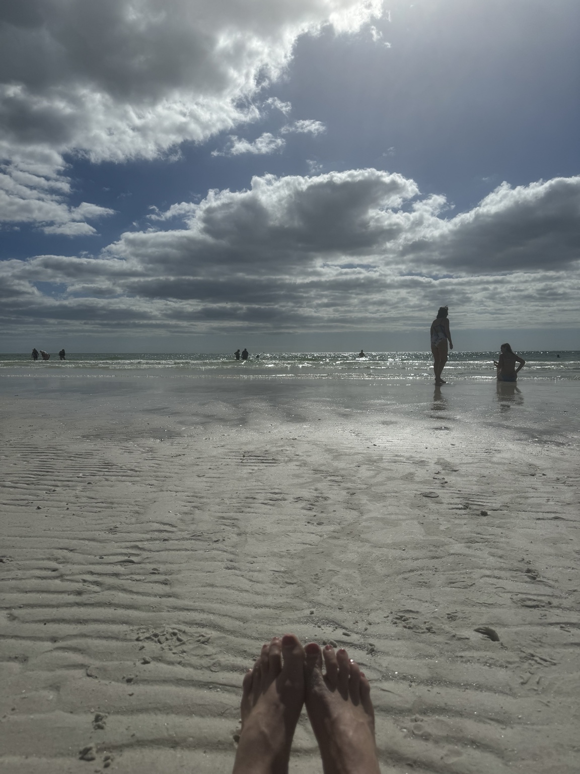 Families playing in the shallow Gulf water beneath a dramatic sky at Siesta Beach