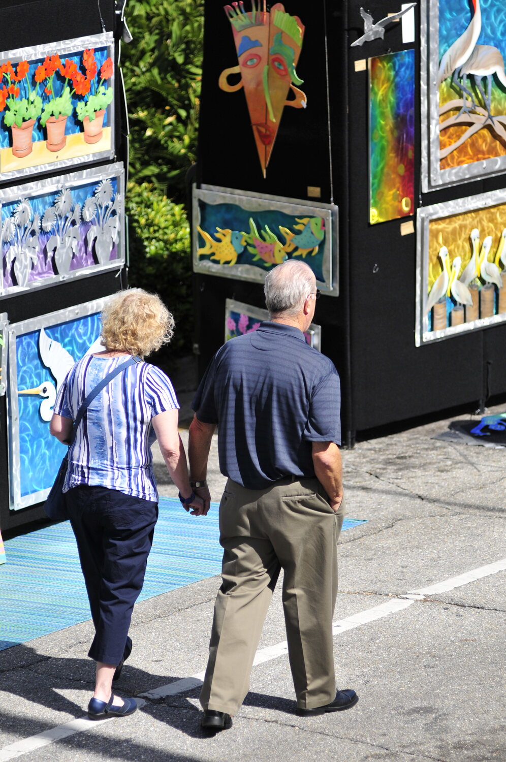 Two visitors browsing a display of colorful paintings and metal art