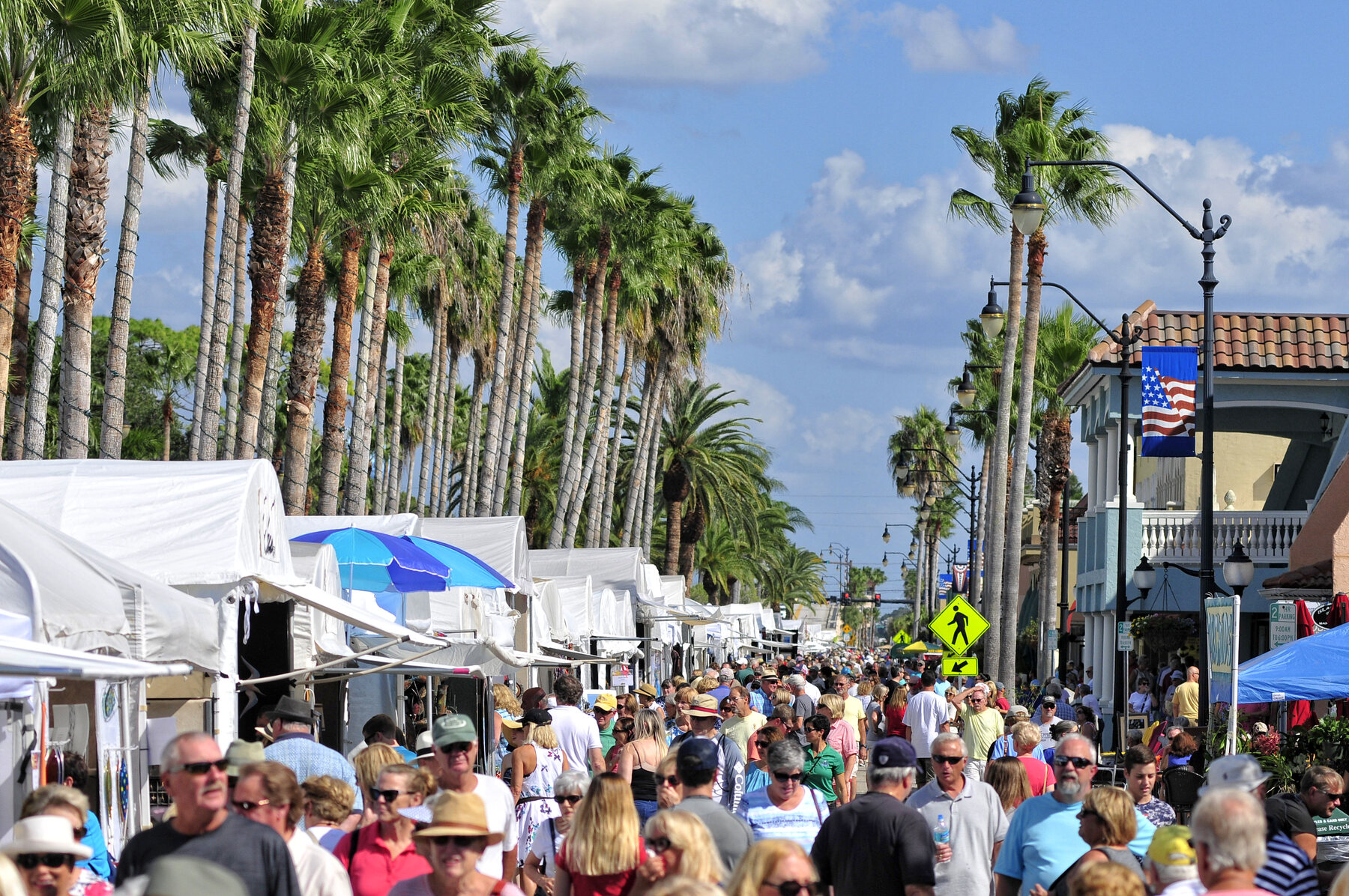 Crowds browsing white art festival tents along palm-lined West Venice Avenue